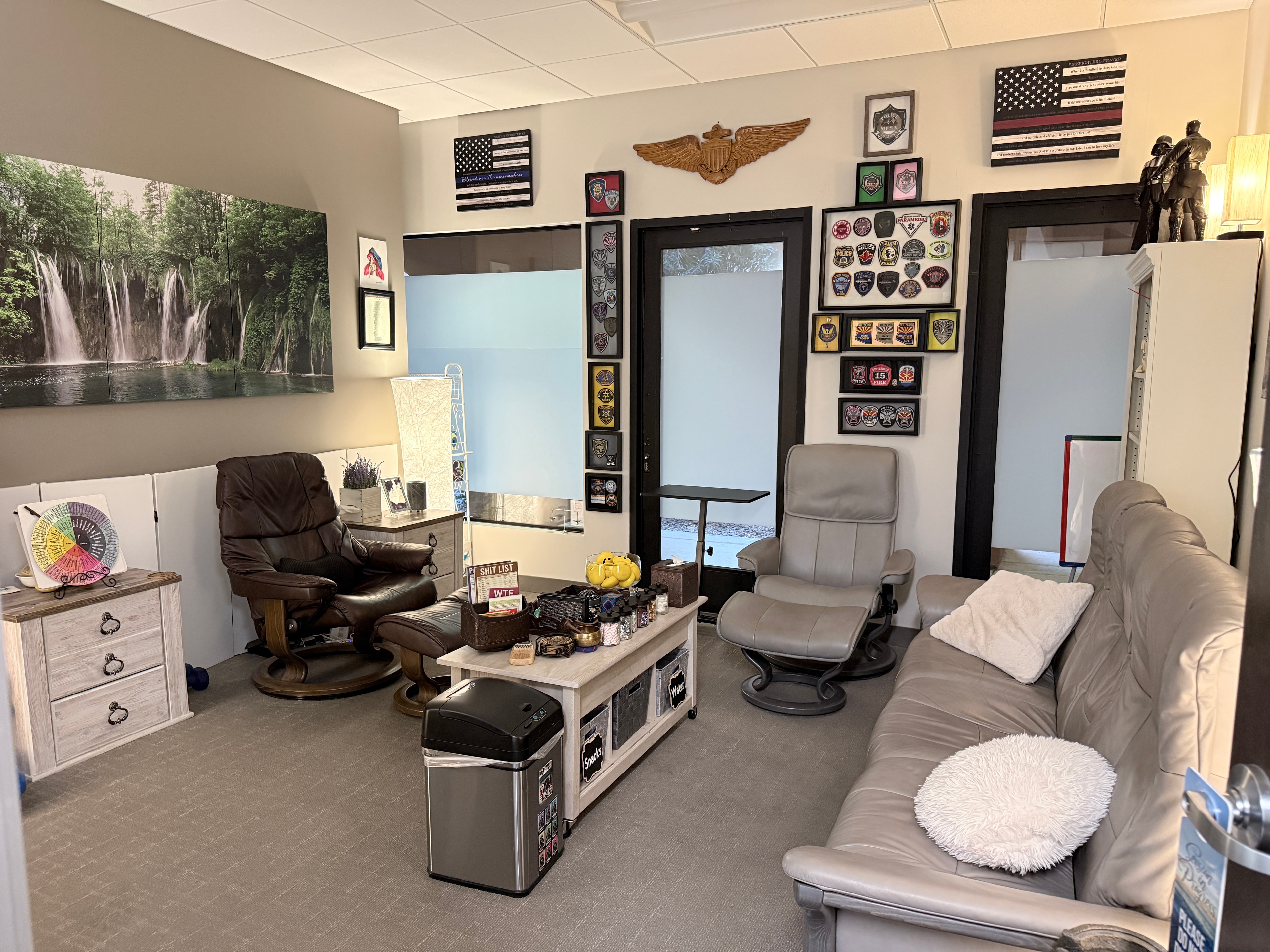 Therapy office with comfortable seating, police badge memorabilia, and a calming waterfall mural